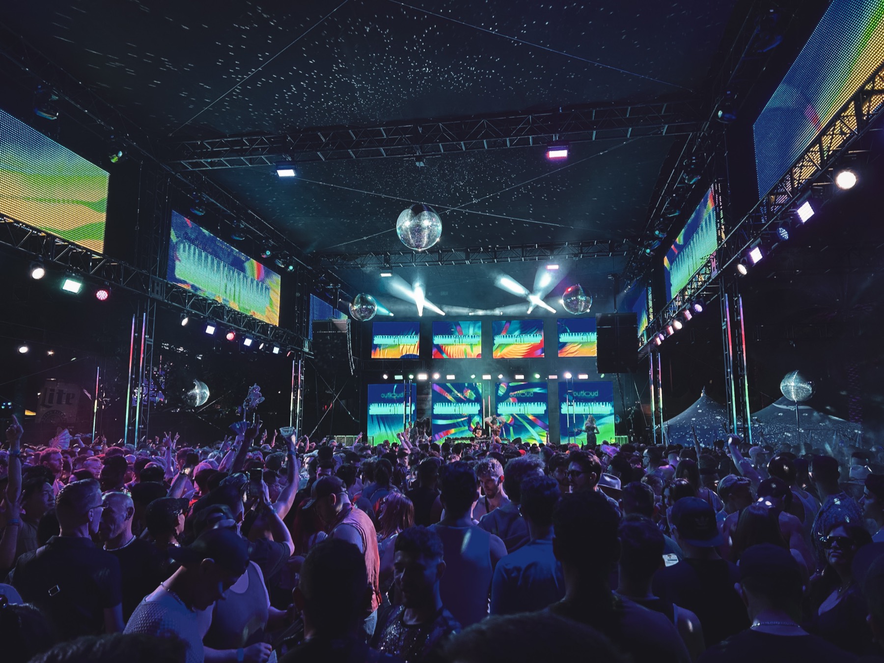 Festival crowd under disco balls with stage video walls