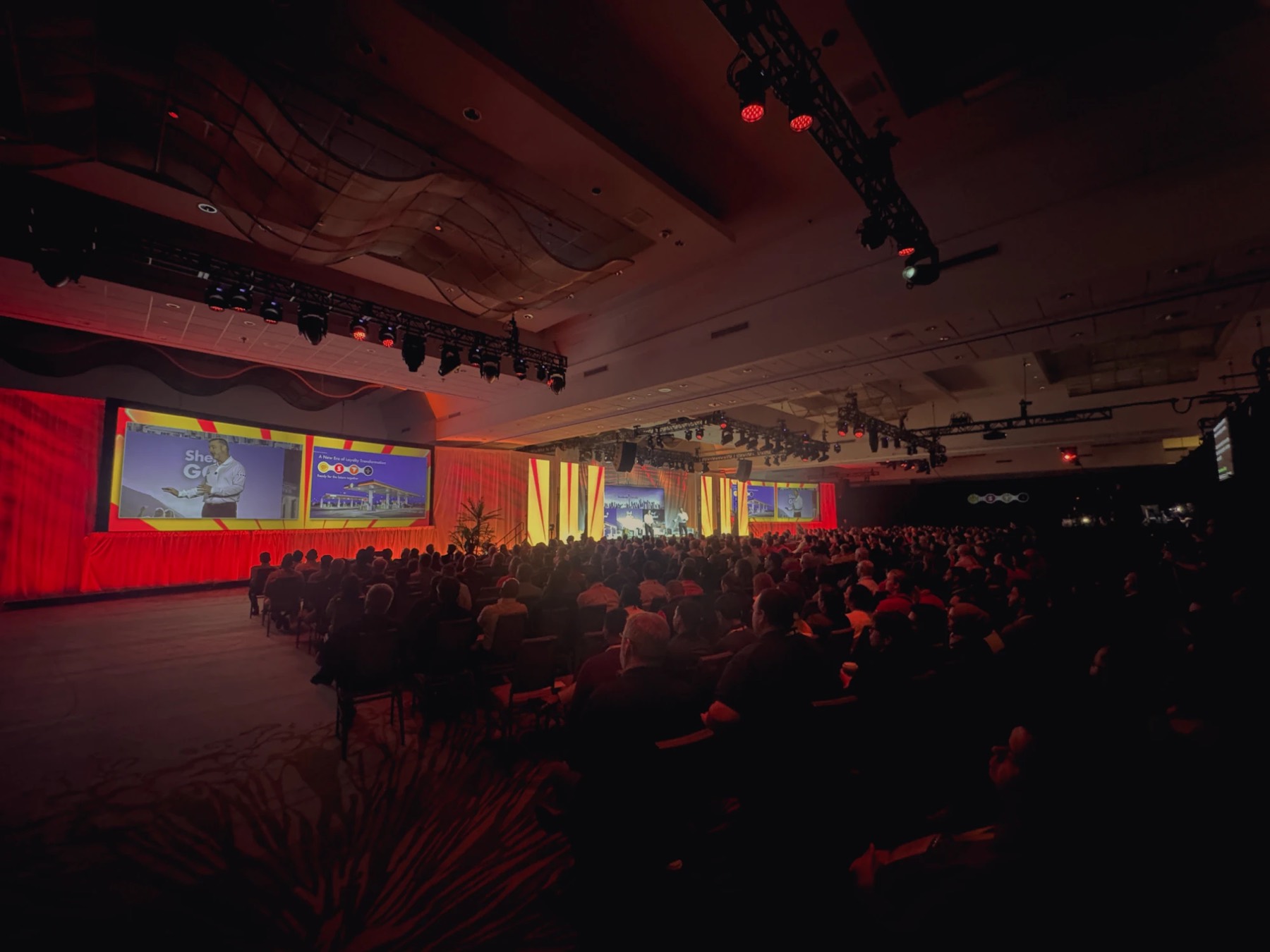 Brand conference with triple screens and red-lit drapery